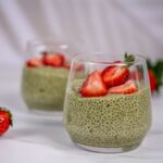 Zwei Gläser veganer Matcha-Chia-Pudding, dekoriert mit frischen Erdbeeren, auf weißem Hintergrund. Gesund und lecker!