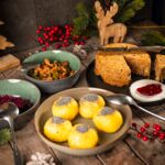 Festlich angerichteter veganer Nussbraten mit Knödeln, Bohnen, Rotkohl und Preiselbeeren auf einem rustikalen Holztisch, umgeben von weihnachtlicher Dekoration.