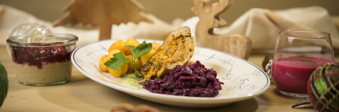 Festliches veganes Weihnachtsessen mit Rotkohl, Kartoffelkroketten und Nussbraten, dekoriert mit Holzfiguren und Beilagen.