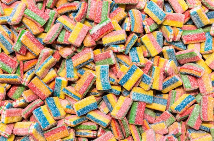 Vegane Süßigkeiten Bunte, gezuckerte, vegane Kaubonbons in Regenbogenfarben, gestapelt in großer Menge – fruchtig, sauer und ohne tierische Inhaltsstoffe.