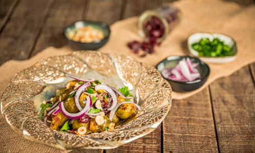 Rosenkohl Pfanne Rosenkohl-Pfanne mit gerösteten Rosenkohlhälften, roten Zwiebelringen, Haselnüssen, getrockneten Cranberrys und frischer Petersilie, serviert auf einem dekorativen, goldfarbenen Teller auf rustikalem Holztisch.