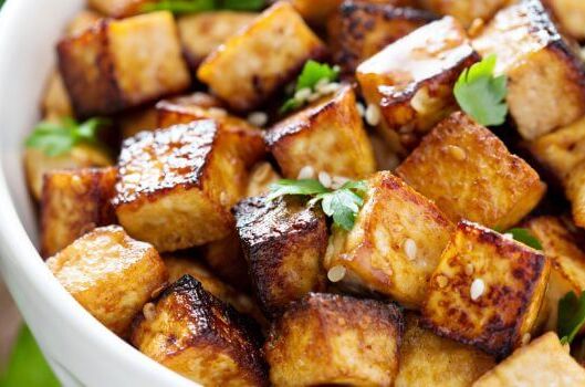 Knuspriges, goldbraun gebratenes Stücke von veganem Tofu, angerichtet in einer Schüssel mit grüner Garnitur. Lecker und gesund!