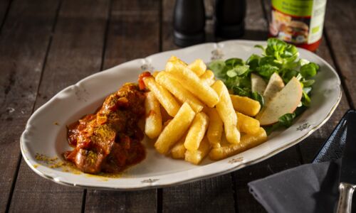 Vegane Currywurst mit Pommes und einem frischen Salat auf einem Teller, perfekt für eine vegane Mahlzeit.