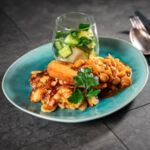 Veganes Schnitzel mit knusprigen Bratkartoffeln, Pilz-Rahm-Sauce und frischem Gurkensalat, dekoriert mit Petersilie auf einem türkisen Teller.