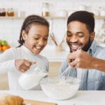 Vater und Tochter backen zusammen mit Milchalternative und haben Spaß in der Küche, perfekte vegane Backidee für die Familie.