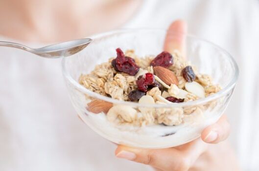 Hand hält eine Schüssel mit veganem Müsli, bestehend aus Nüssen, Mandeln und getrockneten Beeren. Perfekt für einen gesunden Start in den Tag!