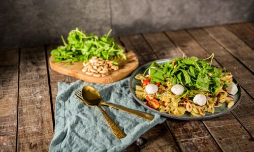 Veganer Nudelsalat mit Rucola, Kirschtomaten und veganer Mozzarella-Alternative auf einem Teller