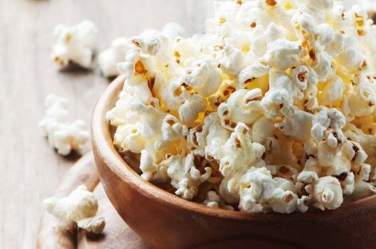 Eine Schüssel mit frischem, weißem, veganem Popcorn auf einem hölzernen Tisch, perfekter Snack für Kinofilme.