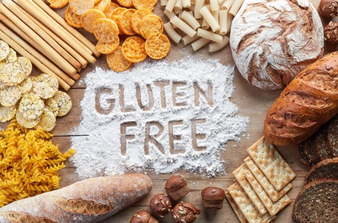 Verschiedene glutenfreie Lebensmittel wie Brot, Reiscracker, Nudeln und Kekse umgeben ein Mehlbett mit der Aufschrift "GLUTEN FREE".