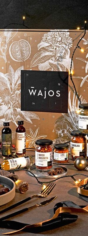 Wajos Gourmet- und Gewürz-Adventskalender in weihnachtlicher Stimmung, umgeben von verschiedenen kulinarischen Produkten, wie Gewürzen, Ölen und Saucen