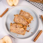 Drei Scheiben veganer Apfel-Zimt-Kuchen auf einem hellblauen Teller, umgeben von Zimtstangen und Apfelhälften. Perfekt für vegane Genussmomente!