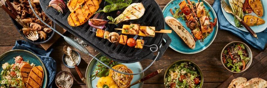 Verschiedene vegane Gerichte, farbenfrohes Grillgemüse und knackige Salate auf blauen Tellern, appetitlich angerichtet für einen perfekten veganen Grillabend.