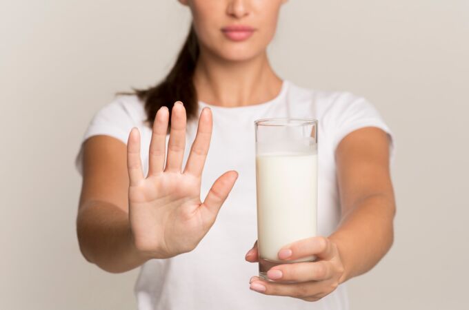 Person in weißem T-Shirt hält Stopp-Geste vor Glas Milch, betont vegane, laktosefreie Lebensmittel; für gesunde Ernährung.