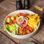 Bunte vegane Bowl mit pflanzlichem Hack, frischem Gemüse und knusprigen Tortilla-Chips, inspiriert von der mexikanischen Küche.