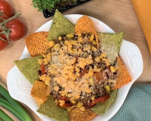 Bunte vegane Tacoauflauf mit Tortilla-Chips, veganem Käse und Gemüse garnieren, ideal für vegane Feinschmecker.