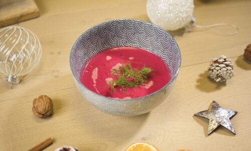 Eine Schale mit veganer Rote-Bete-Suppe, dekoriert mit Dill, umgeben von weihnachtlicher Dekoration. Perfekt für das festliche vegane Weihnachtsmenü!