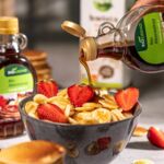 Eine Schale mit veganen Mini-Pancakes, dekoriert mit frischen Erdbeeren und übergossen mit Biogreno Bio Ahornsirup. Ideal für ein köstliches veganes Frühstück!