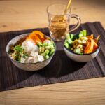 Vegane Glasnudel-Bowl mit Tofu, Karotten, Gurken, Kichererbsen und frischen Kräutern. Perfekte gesunde Mahlzeit! Im Hintergrund ein Glas Eistee.