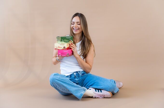 Eileen, Gründerin von Lini's Bites, sitzt lächelnd auf dem Boden und präsentiert vegane Linis Bites Pralinis.