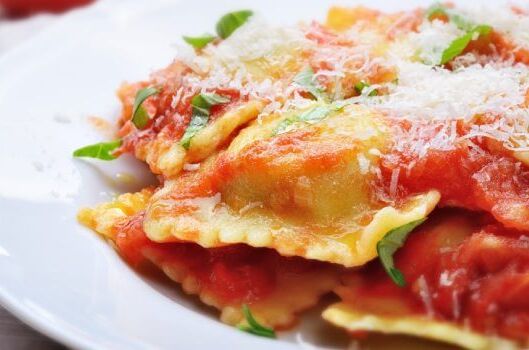 Veganes Fertiggericht mit Ravioli in Tomatensauce, garniert mit frischen Kräutern und veganem Käse, appetitlich auf einem weißen Teller serviert.