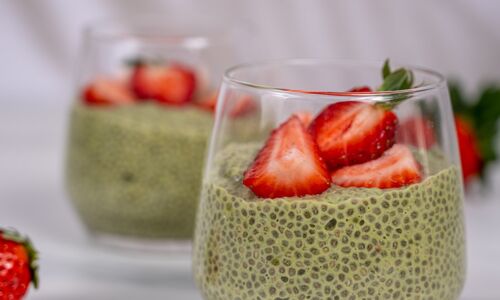 Zwei Gläser veganer Matcha-Chia-Pudding, dekoriert mit frischen Erdbeeren, auf weißem Hintergrund. Gesund und lecker!