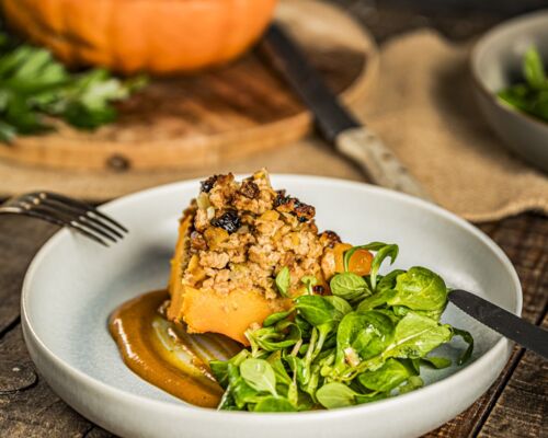Vegan gefüllter Kürbis, serviert mit Kürbisketchup und frischem Feldsalat auf einem Teller. Herbstliches Rezept mit pflanzlicher Hackfüllung.