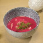 Vegane rote Bete-Suppe in blau-weißer Schale mit Dillgarnitur auf Holztisch, ideales Weihnachtsmenü.