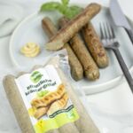 Packung Vegan Leben Pflanzliche Kräuter-Griller vor gegrillten Würstchen mit Besteck und Senf auf einem Teller.