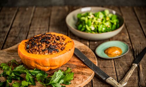 Gefüllter Kürbis: Veganes Ofengericht mit Hokkaido und Hack auf Erbsen-Bohnen-Basis, serviert mit Feldsalat und Kürbisketchup.