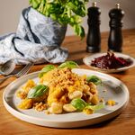 Goldbraun gebratene vegane Gnocchi mit Hokkaido-Kürbissoße, knusprigen Brotbröseln und Basilikum, im Hintergrund ein Rote-Bete-Salat.