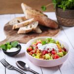 Veganer Linsensalat mit roten Linsen, Gurke, Wassermelone und Sojajoghurt, serviert mit frischem Baguette.