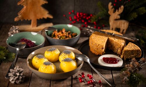 Veganer Braten mit Knödeln, Rotkohl, grünen Bohnen und Preiselbeeren, festlich angerichtet auf einem rustikalen Holztisch mit weihnachtlicher Dekoration.