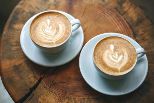 Zwei Tassen mit veganem Cappuccino auf einem Holztisch, mit Herzlatte-Art. Perfekt für einen veganen Genussmoment.