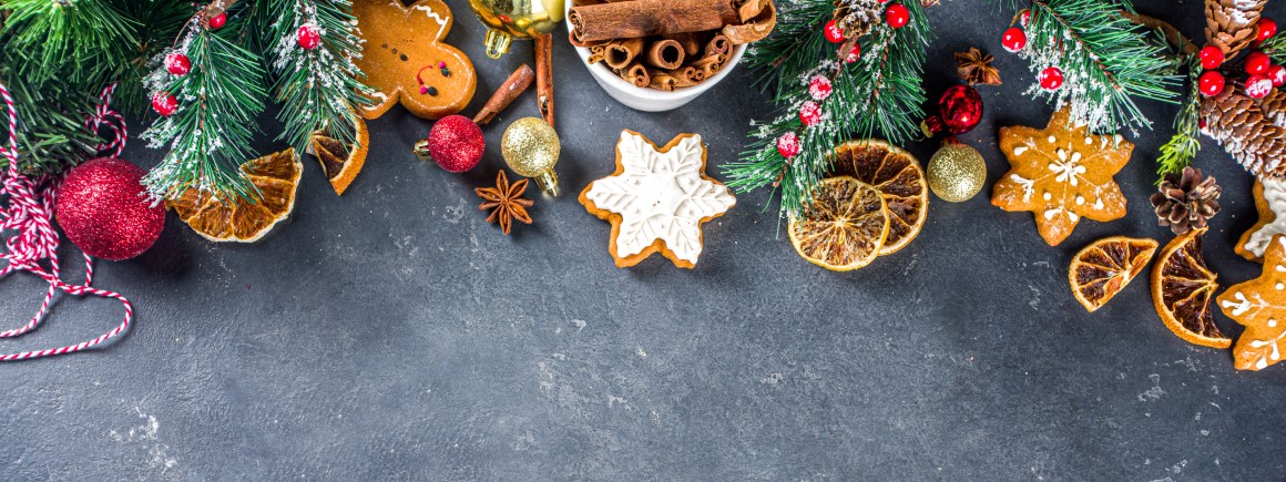 Verschiedene vegane Backzutaten und Weihnachtsdekoration auf einem Tisch, darunter Zimt, getrocknete Orangen, Lebkuchen und Tannenzweige – perfekt für veganes Weihnachtsgebäck!