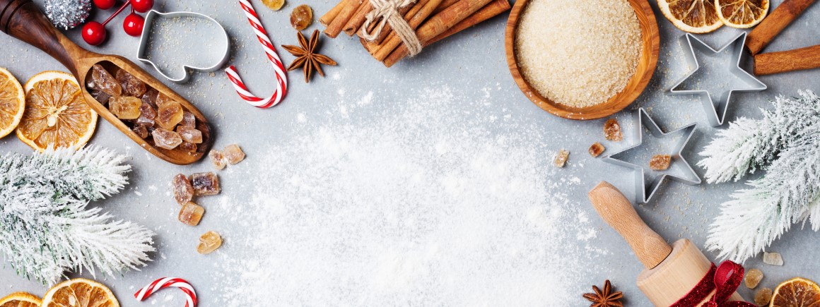 Fröhlich dekorierte vegane Weihnachtsbäckerei mit Backzutaten wie Zimt, Zucker, getrocknete Orangenscheiben und Zuckerstangen.