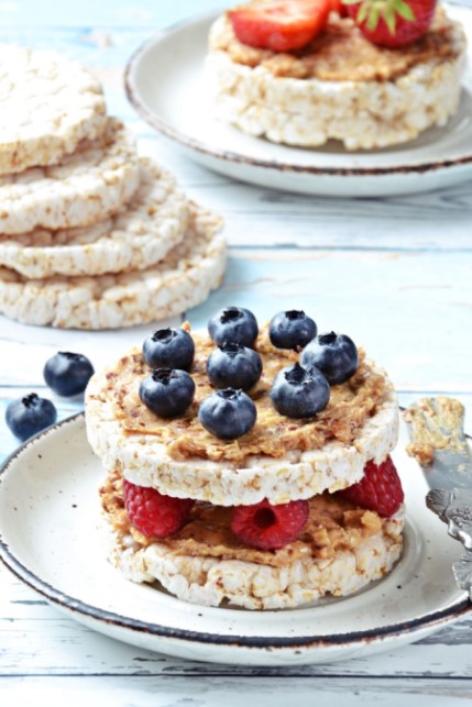 Ein Teller mit einer Reiswaffel, belegt mit Erdnussbutter, Heidelbeeren und Himbeeren. Ideal für vegane Snacks dank leckerer Erdnussbutter!