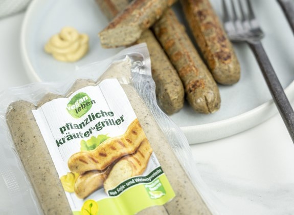 Zwei Packungen "Pflanzliche Kräuter-Griller" der Marke Vegane Welt auf einem weißen Teller mit Senfklecks, perfekt für den veganen Genuss.