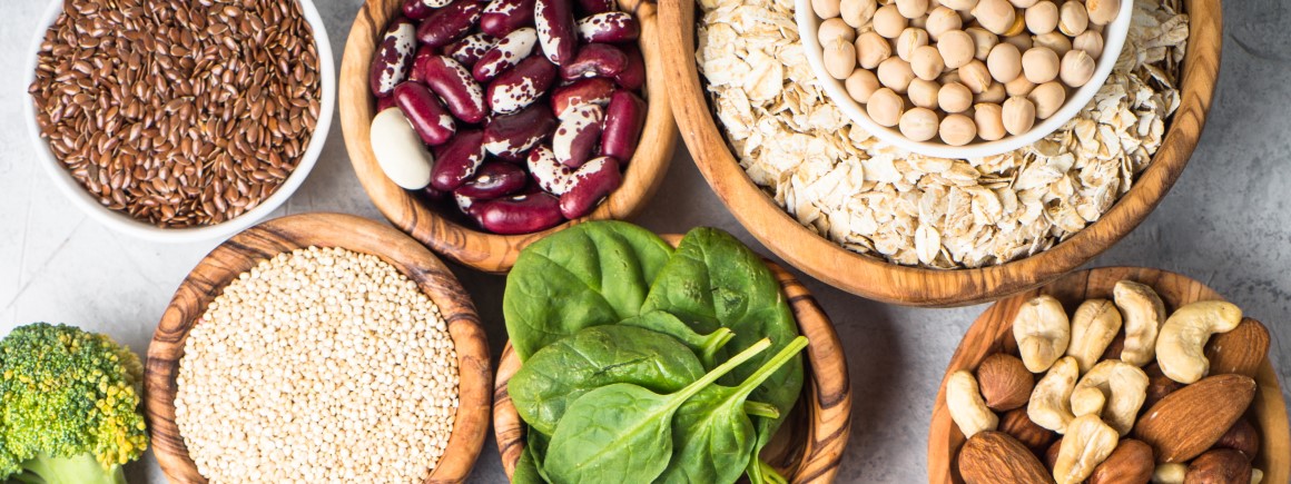 Verschiedene vegane eisenreiche Lebensmittel wie Spinat, Bohnen, Nüsse, Quinoa, Brokkoli und Haferflocken in Holzschalen.