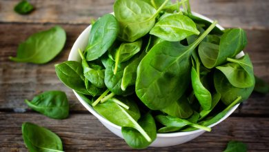 Weiße Schüssel gefüllt mit frischen grünen Spinatblättern, auf grobem Holztisch für vegane Ernährung.