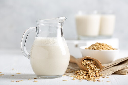 Karaffe mit frischer, cremiger Hafermilch neben einer Schale voller Haferflocken auf einem hellen Tisch. Perfekt für gesundes, veganes Backen!