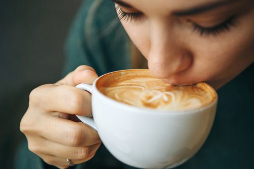 Nahaufnahme einer Frau, die genussvoll eine Tasse Kaffee mit veganer Milch trinkt. Perfekt für den veganen Lebensstil!